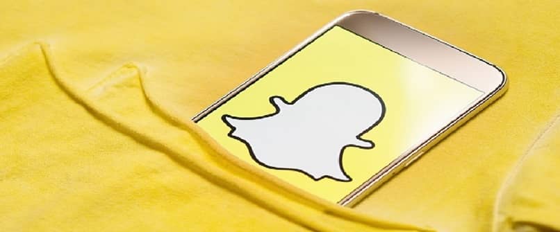 El fondo amarillo indica desde un bolsillo un teléfono móvil con el logo de Snapchat