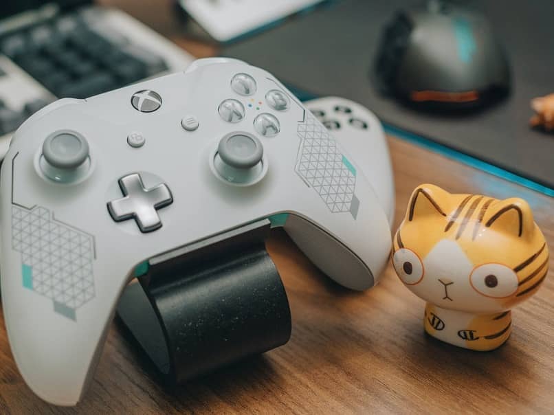 Controlador de videojuegos de la marca xboxlive blanco en el escritorio junto a la muñeca de gato a rayas